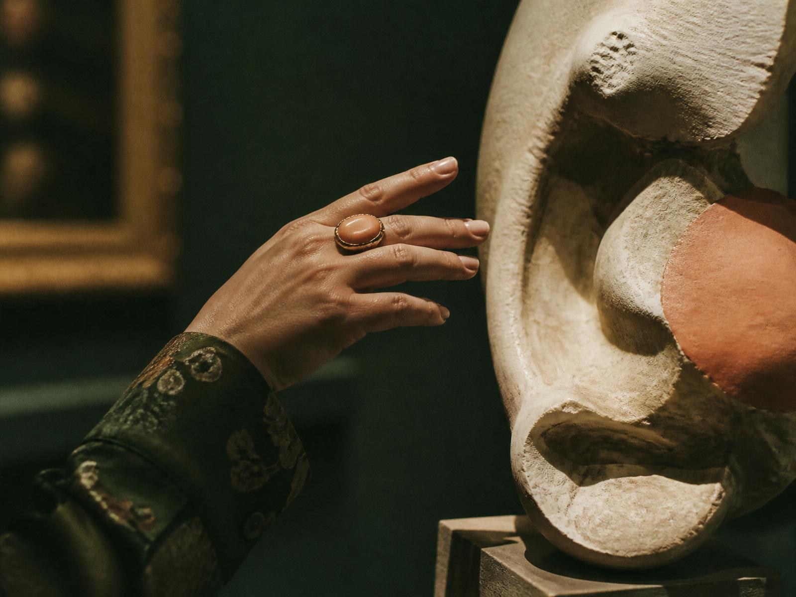 Hand reaching toward a sculptural artwork in a moody gallery